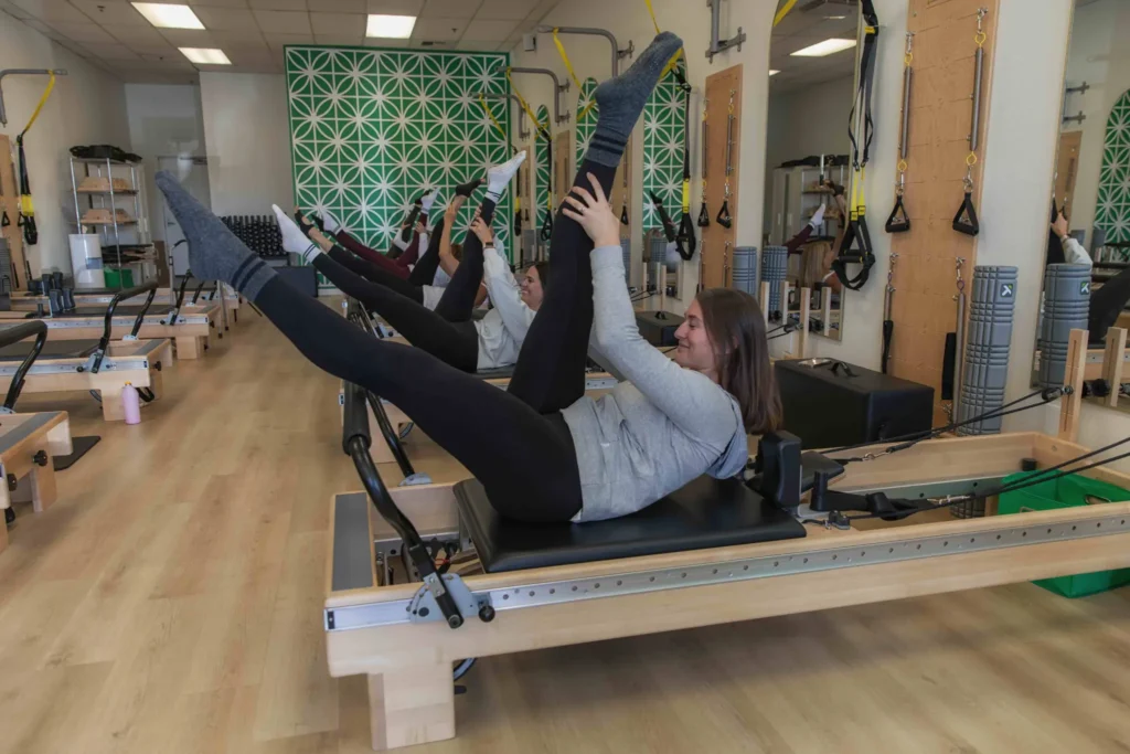 Women stretching their legs during a group Pilates reformer class in a modern studio.