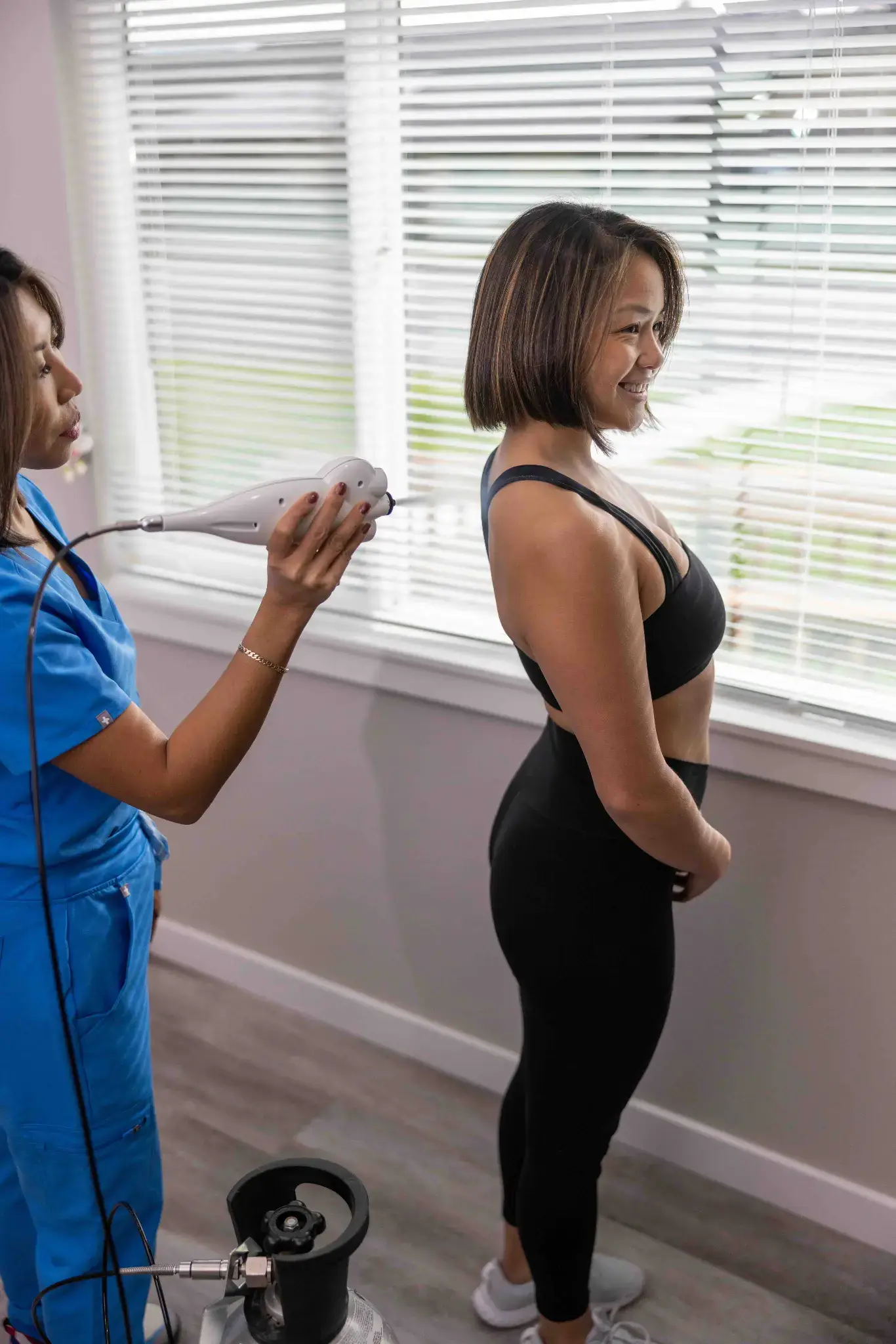 Practitioner in blue scrubs applying localized cryotherapy to a smiling woman's back.